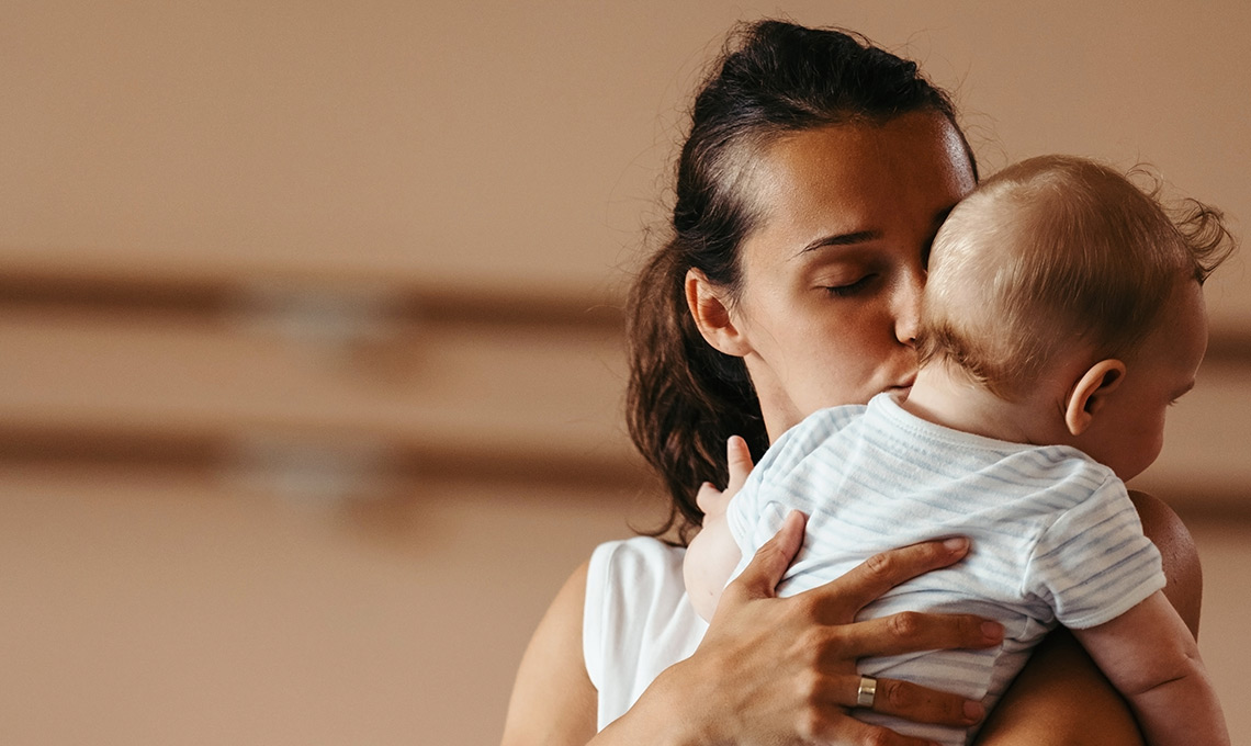 Mutter küsst Baby in ihrem Arm - symbolisch für enge Bindung zum Neugeborenen