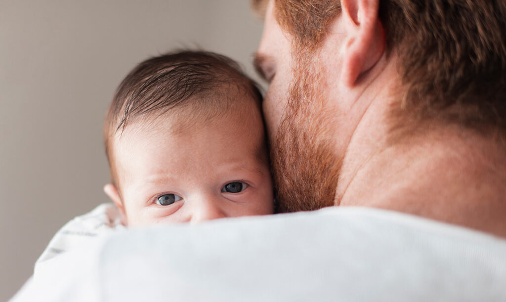 Vater küsst Neugeborenes in seinem Arm - symbolisch für High-Need Baby