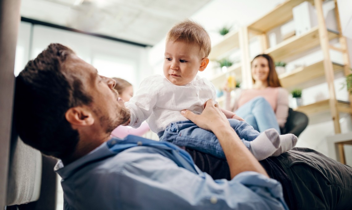Familienszene: Vater spielerisch mit Baby am Boden - als Symbol für Bindung und Beziehung