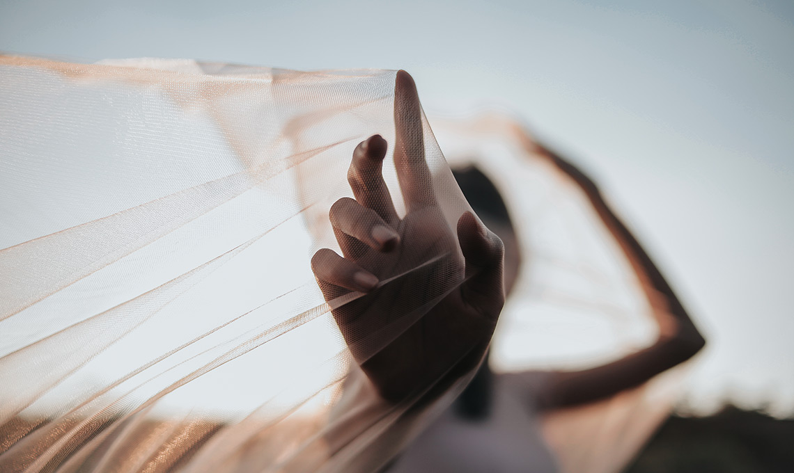 verschwommenes Foto einer Frau mit einem transparentem Tuch spielerisch über Armen und Kopf